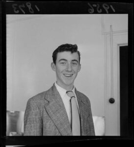 Three-quarter photograph of Jon Trimmer in 1956, wearing a jacket and tie, smiling to the camera.Dancer, Jon Trimmer. Evening post (Newspaper. 1865-2002) :Photographic negatives and prints of the Evening Post newspaper. Ref: EP/1956/1873-F. Alexander Turnbull Library, Wellington, New Zealand. /records/22327700