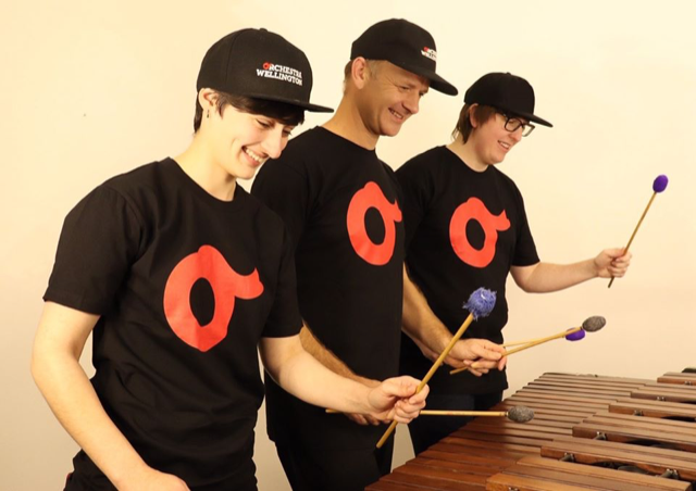 Three musicians, smiling, playing a marimba with 6 wooden mallets