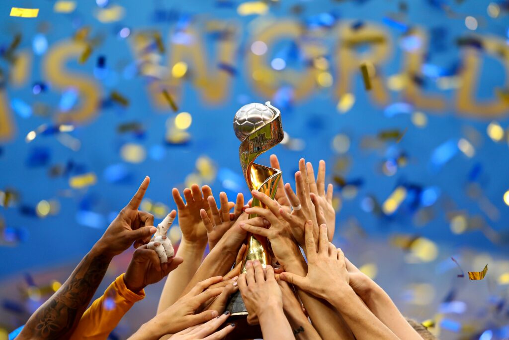 Image of a number of hands raising the FIFA trophy into the air.