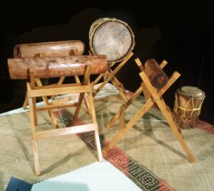 A collection of wooden and skin drums arranged on a woven mat.