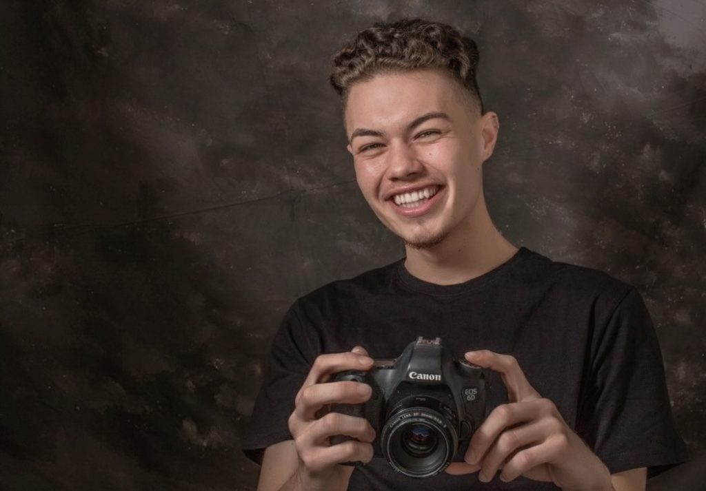 Photo of a smiling young man holding a DSLR camera