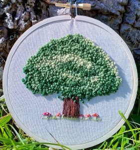 Image shows a hoop embroider, featuring a tree surrounded by small mushrooms on white calico