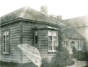Black and white photograph of a weatherboard house. A burred shape appears in the lower left hand side.