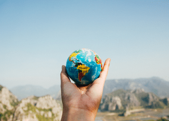 Image of a hand holding a small globe in front of a mountain landscape.