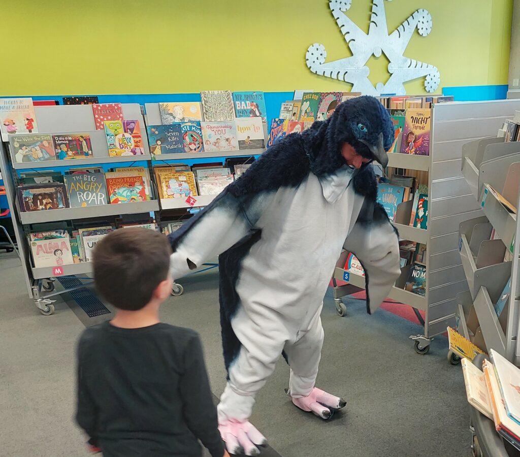 Man walks wearing a kororā penguin suit, child watches.