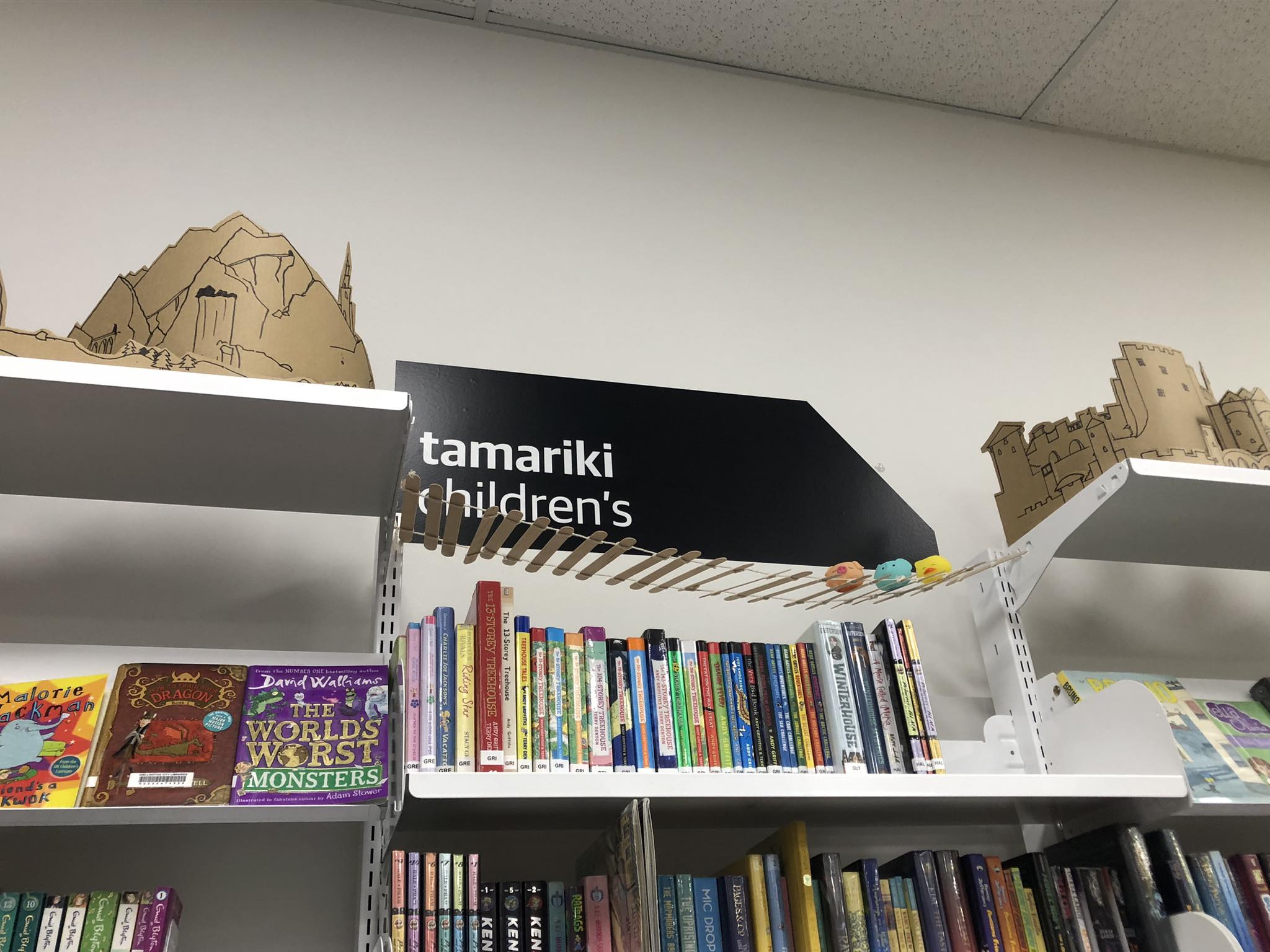 A rope bridge made of twine and popsicle sticks bridges the gap between two bookshelves.