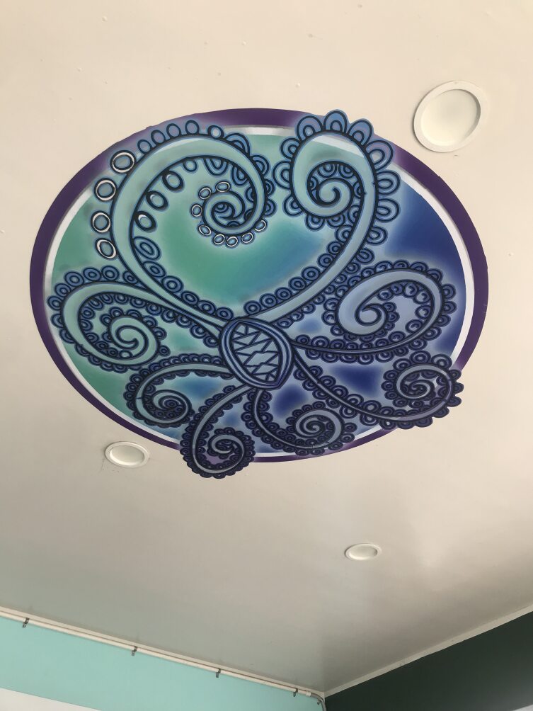A round, curved, three-dimensional artwork on the ceiling. Shades of blue, with koru like tentacles reaching out from the centre.