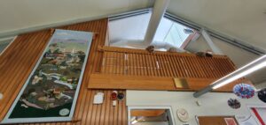 Natural wood balcony with stuffed aniimals liiking down, a skylight above, and long tapestry hanging to the left.