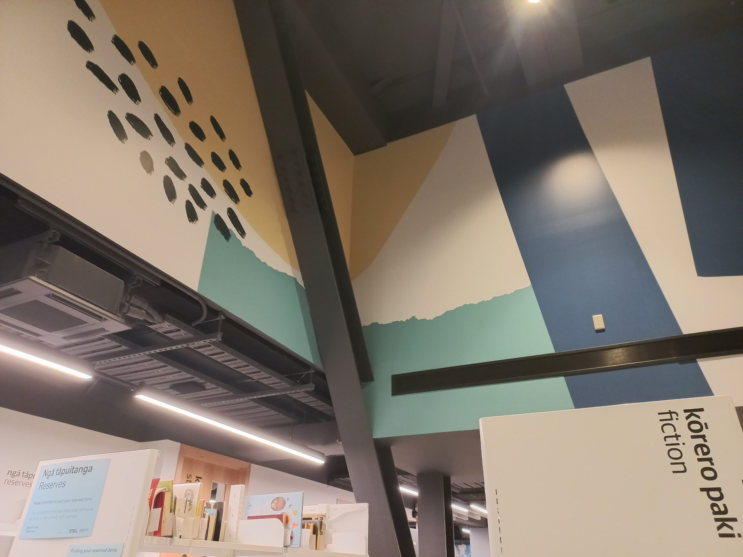 Diagonal industrial beam cuts across decorated upper walls above fiction shelves