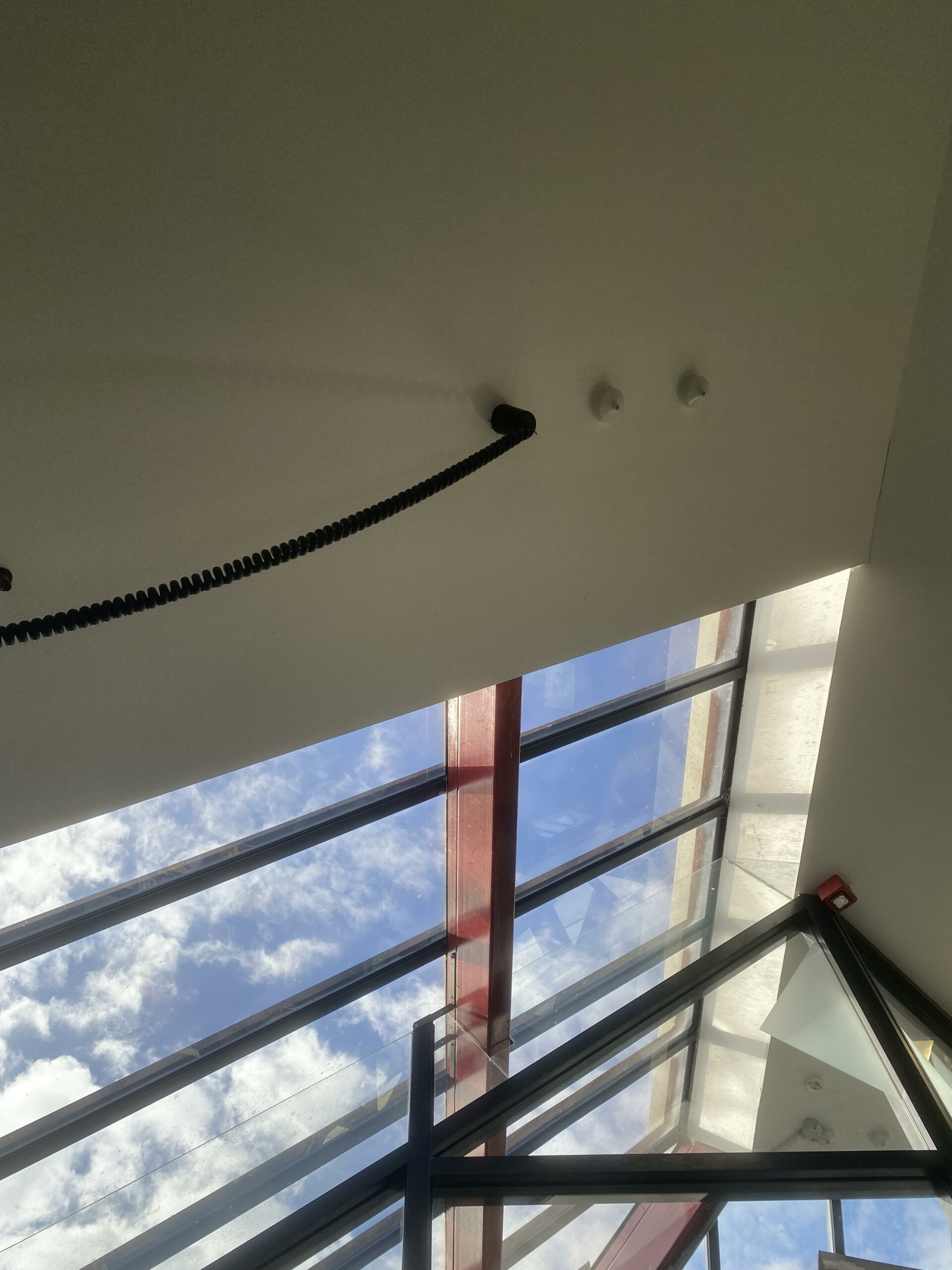 A spiral cord hangs next to a skylight with a red beam across it. Blue sky with fluffy clouds outside.